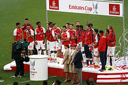 A coloured photograph of the Arsenal squad standing on a podium, celebrating their fourth win.