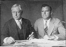 Photograph taken circa 1930 of Burnham with his son Roderick. Frederick Burnham is on the left, and Roderick Burnham is on the right. Both men are wearing suits and ties and they seated at a table with many papers in front of them.