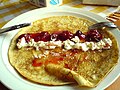 A sweet crêpe opened up, with whipped cream and strawberry sauce on it