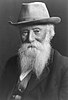 Black and white portrait of an older, bearded man wearing a suit and a hat