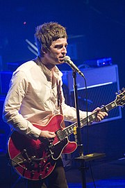 An old man wearing a white shirt performs with a microphone and guitar