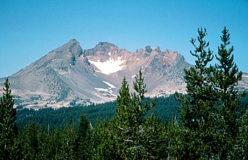 A volcano with a large crater rises above a forested region.