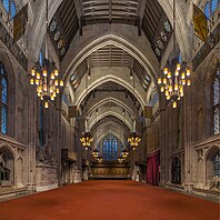 A large medieval hall with pointed arches and a red carpet