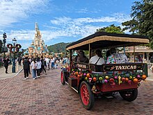 A red and black turn-of-the-20th-century-style taxi on a brick road heading towards a castle