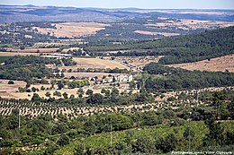 Paysage méditerranée de collines boisées et cultivées, au centre duquel est visible une abbaye.