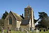 Stone building with arched windows and square tower. In the foreground is a grass area with gravestones.