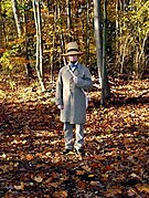 Richard Smith in costume as Henry David Thoreau, standing on autumn leaves near some trees.jpg