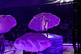 Taylor Swift performs on stage with three purple clouds around her