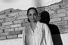 A black and white portrait of the artist Syowia Kyambi. Hair braided, white blouse with dark suspenders, smiling.