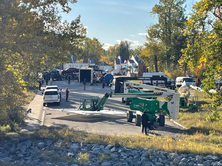 Distant buildings surrounded by trees, with several vehicles, cranes, and people in the foreground.