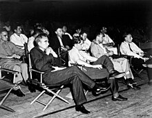 A group of men in shirtsleeves sitting on folding chairs.