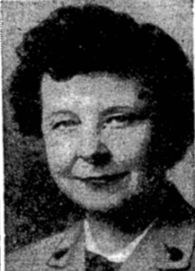 A white woman with fair skin and dark hair wearing a Girl Scout of USA adult uniform with metal buttons