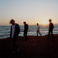 Four men walking on a beach with waves and the sun setting in the distance