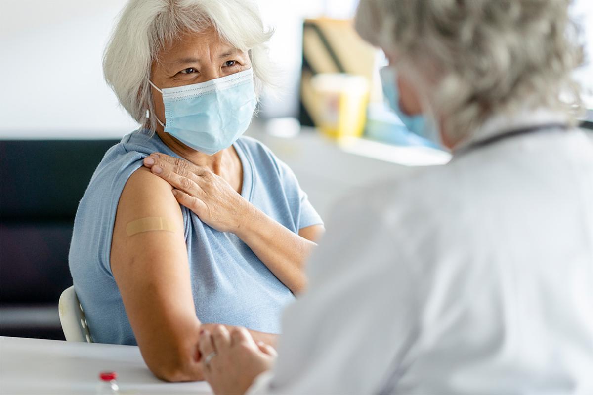 Senior patient holds up her sleeve and smiles as she looks up at her doctor 