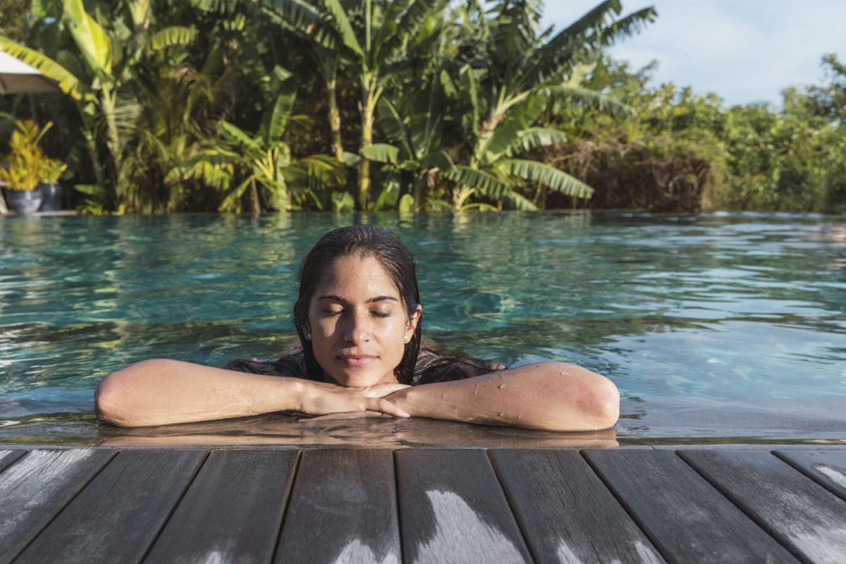 Woman with eyes closed at a tropical resort with palm trees in background