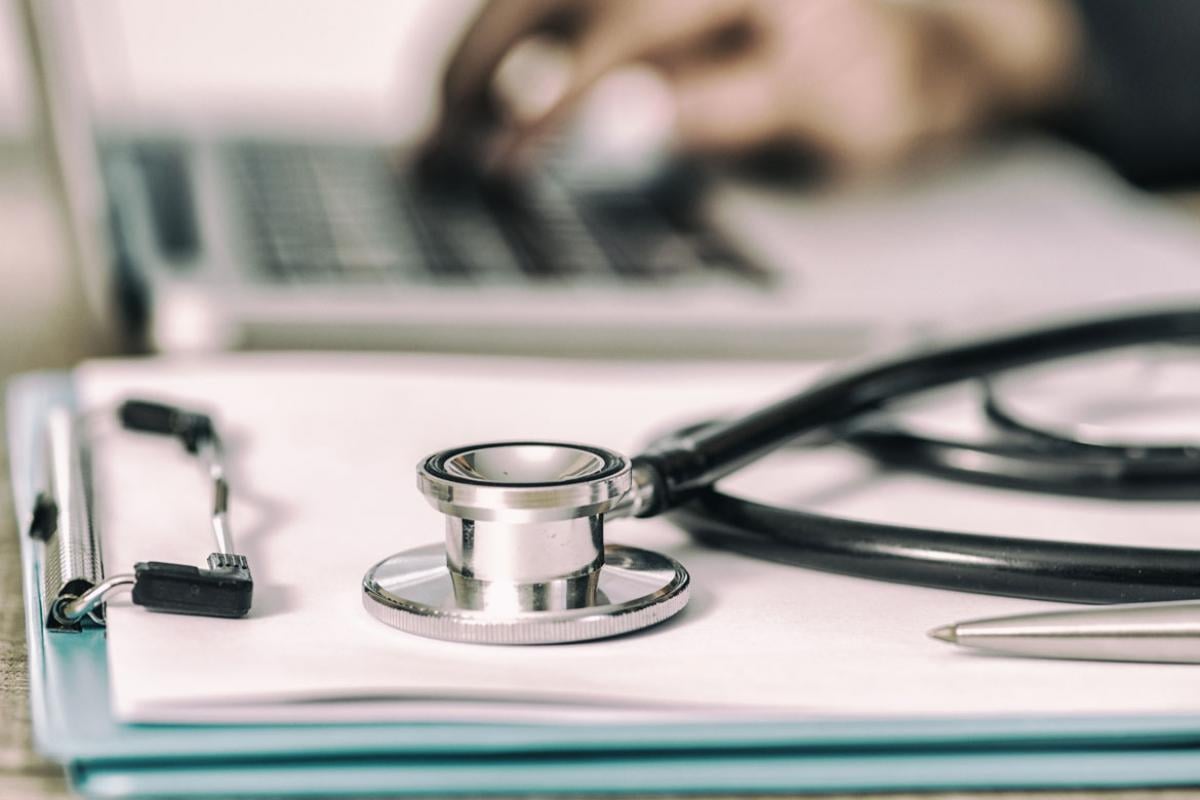 Stethoscope on a clipboard with a hand using a computer mouse