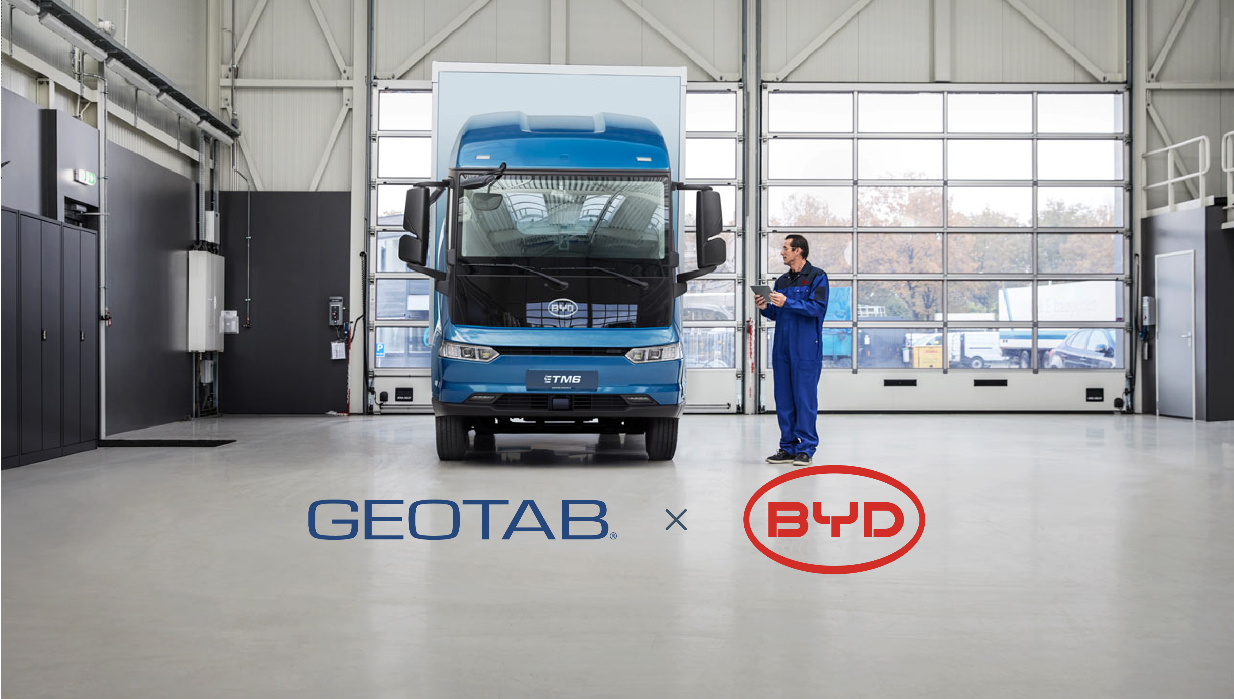 Mezzo pesante elettrico della BYD all'interno di un deposito con un operaio accanto e i loghi Geotab e BYD sotto