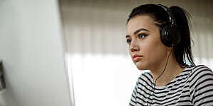 Young woman with headphones looks absorbed as she participates in a distance-learning course.