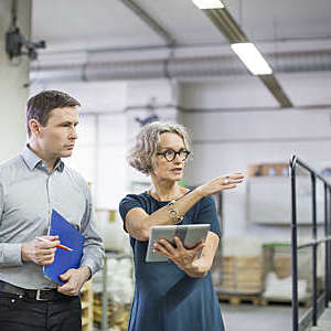 Manager discussing with male worker at printing plant. Professionals with digital tablet and clipboard at printing press.