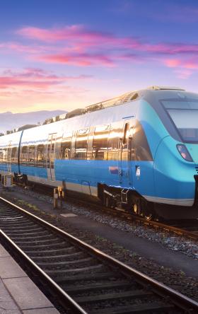 Stock image of a blue passenger train on tracks with pink and purple sunset