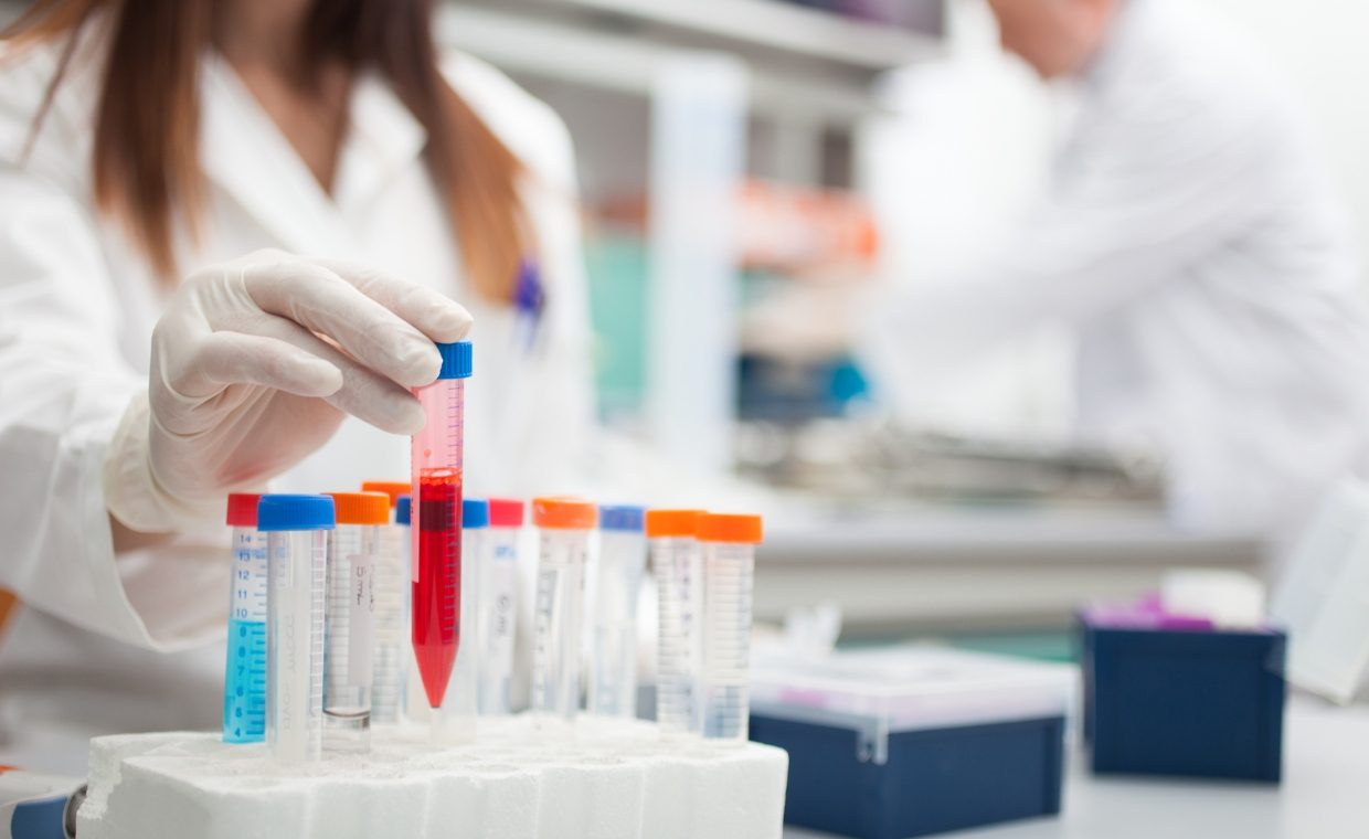 Woman in a white lab coat putting a test tube filled with red liquid in a test tube rack