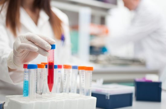 Woman in a white lab coat putting a test tube filled with red liquid in a test tube rack