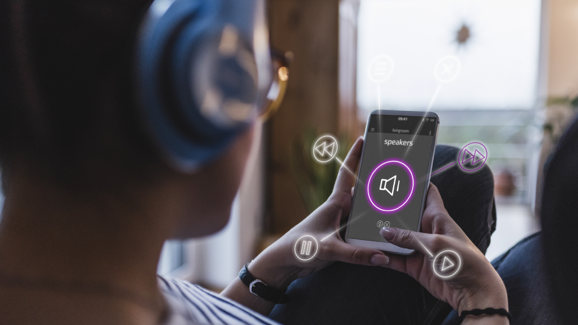 A person with headphones on, using a mobile device to wirelessly control speakers