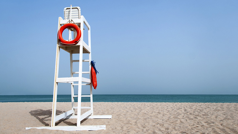 White life guard tower with a red life ring on a beach.