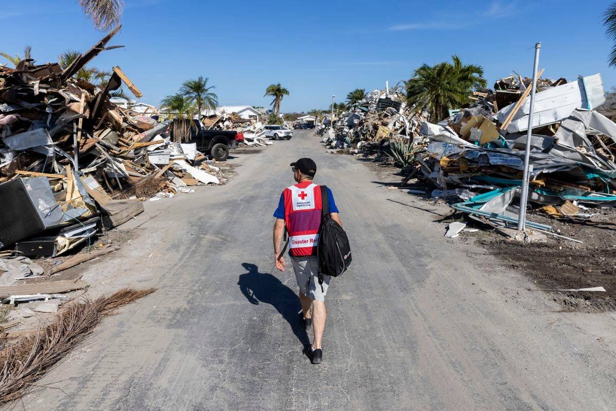 A Red Cross disaster volunteer is walking down a street that has been devastated by a natural disaster