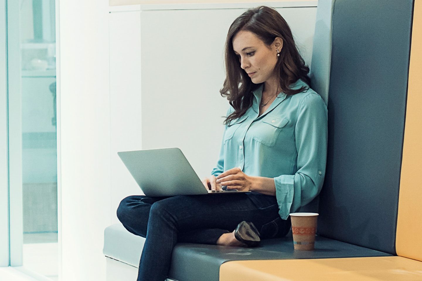 Jonge vrouw met laptop op haar schoot in een verlichte kantoorruimte