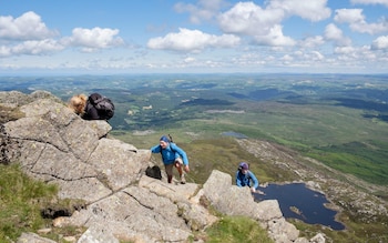 Three hikers scrambling up rocks on Carnedd Moel Siabod Daear Ddu east ridge with view down to Llyn y Foel Snowdonia National Park (Eryri) Wales UK