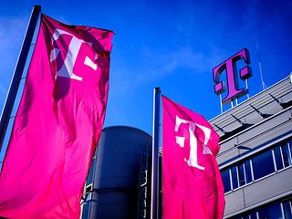 View of a Deutsche Telekom building with a large Deutsche Telekom logo and magenta flags against a blue sky