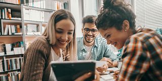 Young people sit happily together and work together on the tablet.