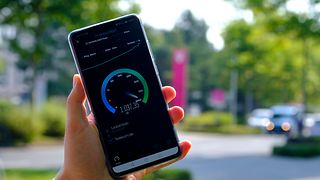 Blurred background, with a Telekom employee holding a smartphone, displaying a 5G network speed test.