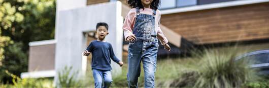 Brother and sister running in front yard of modern home.