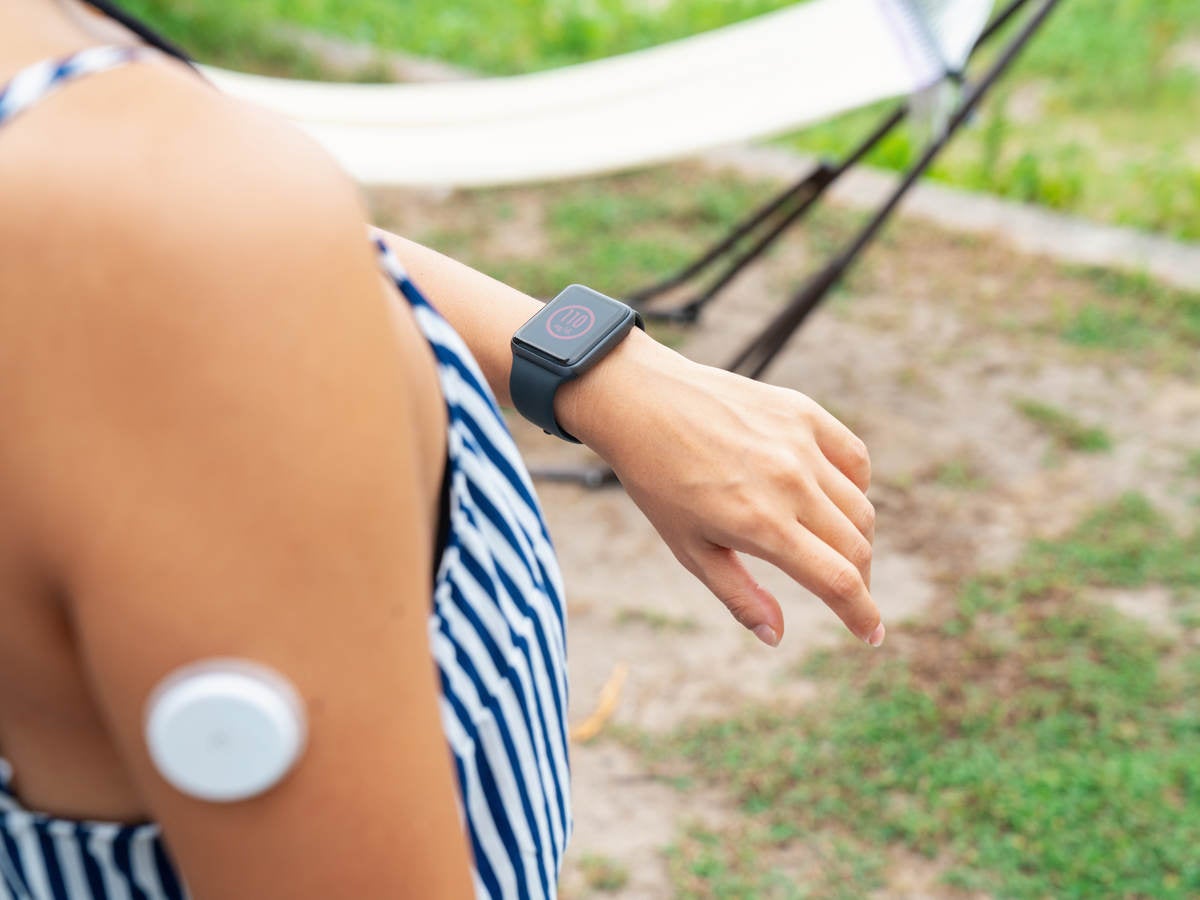 Young woman with wearable patch on arm checking a smartwatch to see her blood sugar level.