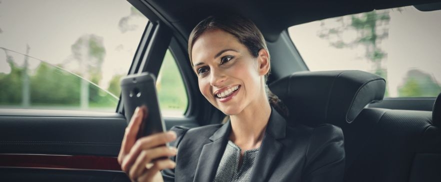 Frau, die im Auto sitzt und auf ihr Handy schaut