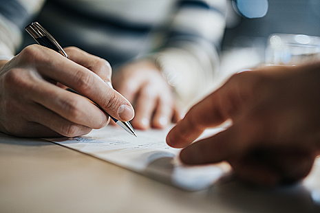 two hands, one holding a pen, pointing at a document