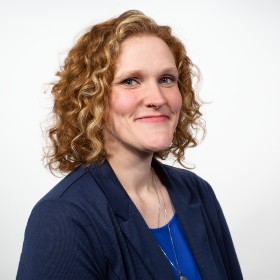 Kristen McGrath - White woman with curly red hair and a blue jacket