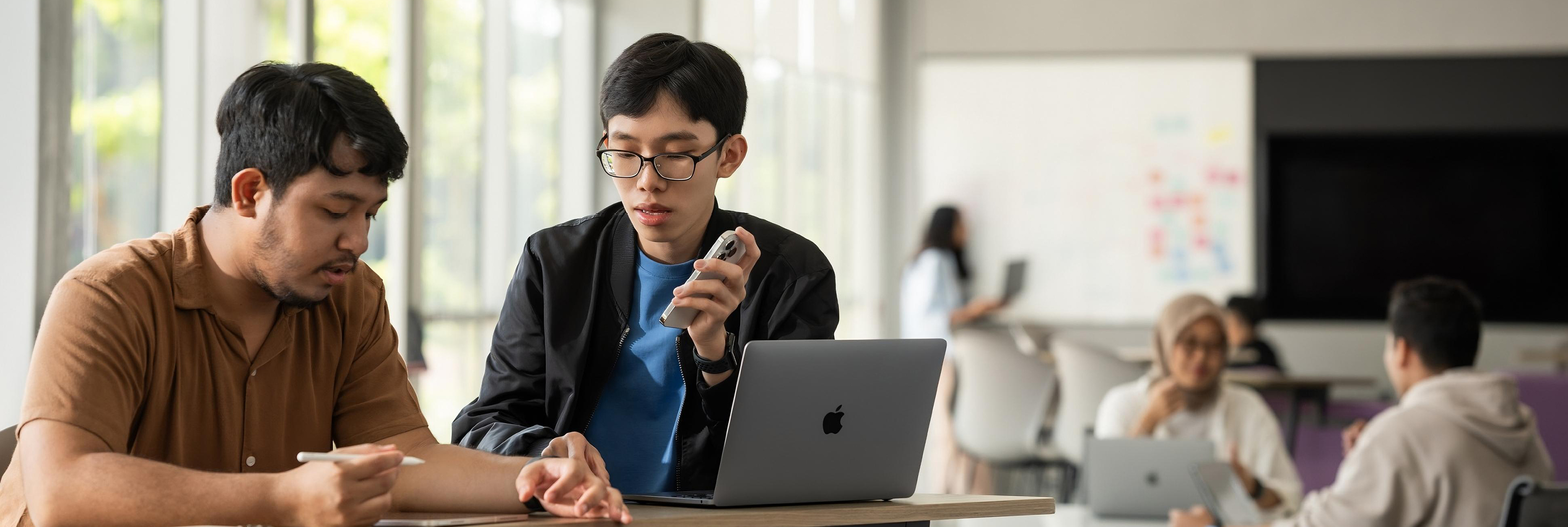 情報技術科の学生であり、Apple Developer AcademyのメンターでもあるJia Chenさんが、iPhoneとMacBookを使って、オープンワークスペースで仲間と共同作業している。