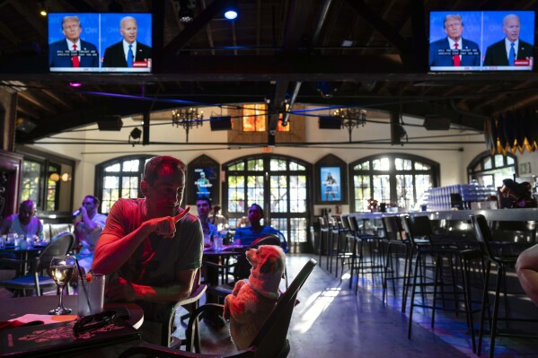 Michael Fossat signals to his dog, Myla Zane, to stand still while watching a presidential debate between President Joe Biden and Republican presidential candidate, former President Donald Trump, at the Abbey Food & Bar in West Hollywood, Calif., Thursday, June 27, 2024. (AP Photo/Jae C. Hong)