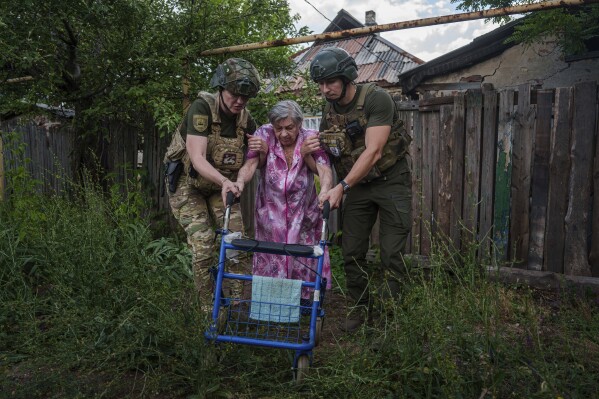 Police officers of the White Angels unit help an elderly woman walk into a van during an evacuation to safe areas, in Toretsk, Donetsk region, Ukraine, Friday, June 28, 2024. (AP Photo/Evgeniy Maloletka)