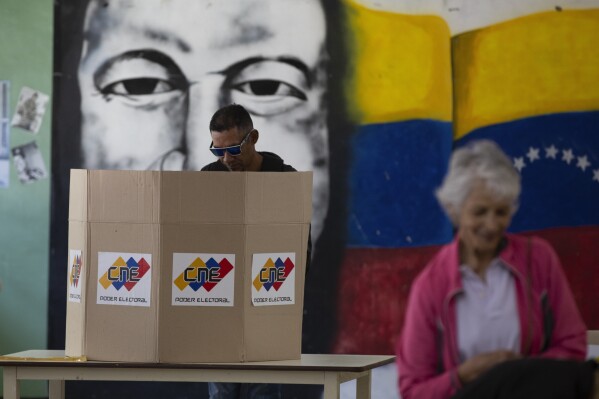 A man casts his ballot in front of a mural of late President Hugo Chavez as part of a rehearsal for the July 28 presidential election at a voting center in Caracas, Venezuela, Sunday, June 30, 2024. (AP Photo/Cristian Hernandez Fortune)
