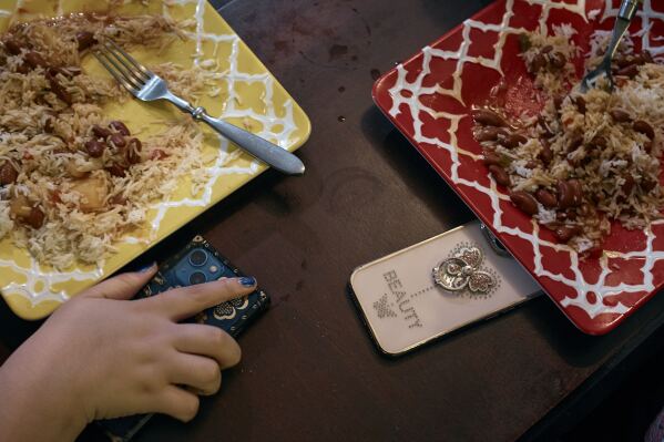 Gionna Durham, 13 , left, holds her phone as she has dinner with her sister Gabriela Durham, 17 years old, unseen, on Saturday, Jan. 27, 2024, in New York. Concerns about children and phone use are not new. But there is a growing realization among experts that the COVID-19 pandemic fundamentally changed the relationship kids have with social media. As youth coped with isolation and spent excessive time online, the pandemic effectively carved out a much larger space for social media in the lives of American children. (AP Photo/Andres Kudacki)