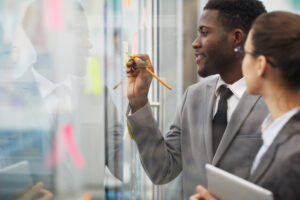 Two coworkers writing notes on a glass wall