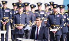 Rishi Sunak speaks at the D-Day 80th anniversary event in Normandy; soldiers in dress uniform are seen standing behind him.