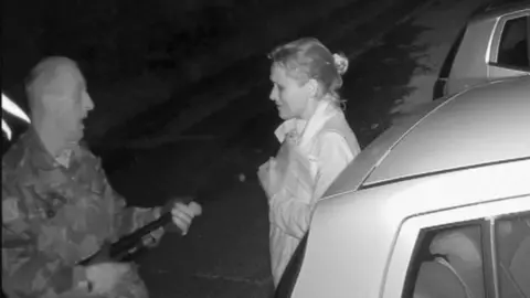 Black and white CCTV footage of a man with a gun pointed at a woman