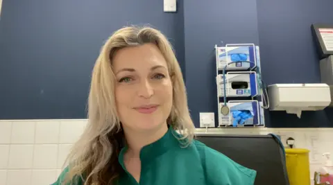 Woman with green top sitting in a veterinary surgery looking at the camera