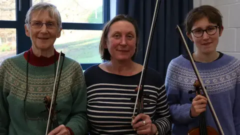 Miranda Wilson, Anna Wilson and Astrid Wilson-Gignoux holding their violins and smiling