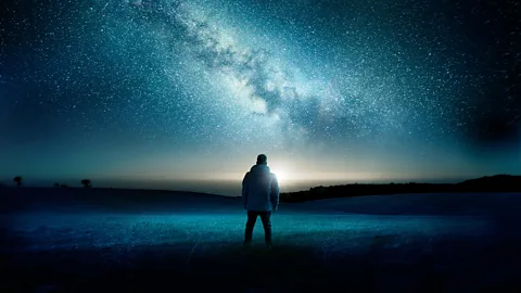 Man by the water looking at starry sky (Credit: Alamy)